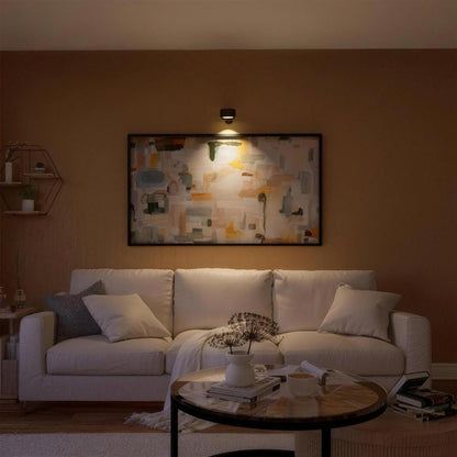 Black Nook lamp lighting a painting above a living room sofa
