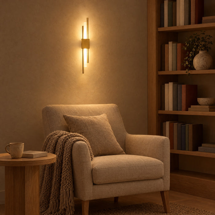 A gold Nook Duo Sconce above an armchair in a reading corner