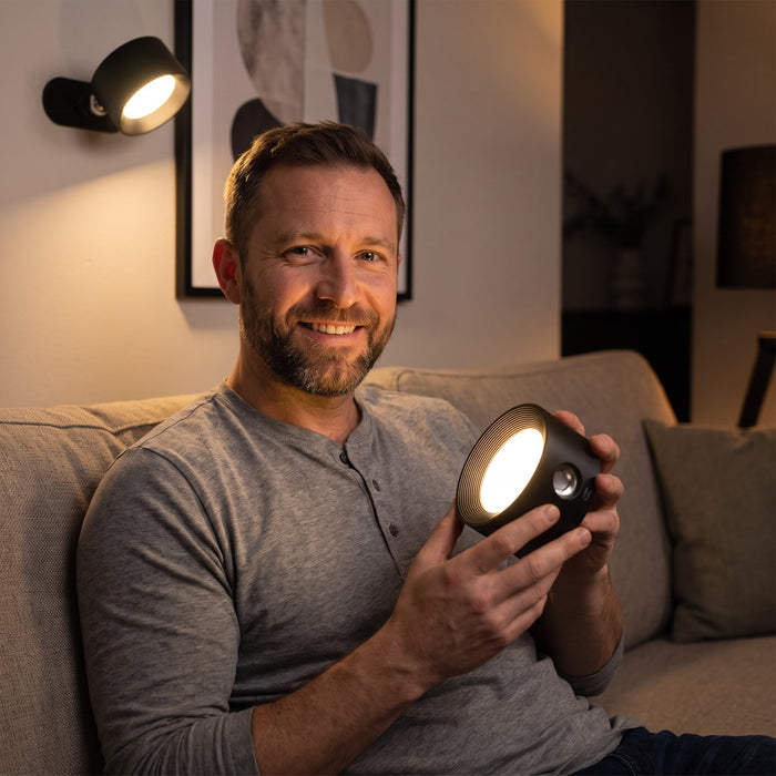 Man on a sofa holding the black Nook lamp