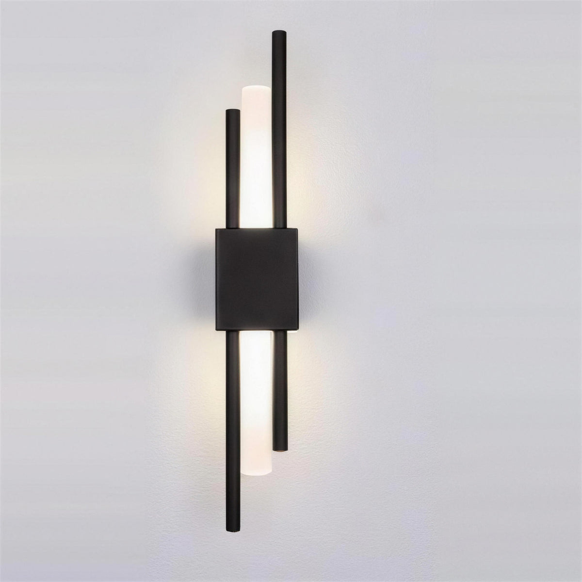 Nook Duo Sconce in black, lit on a grey wall